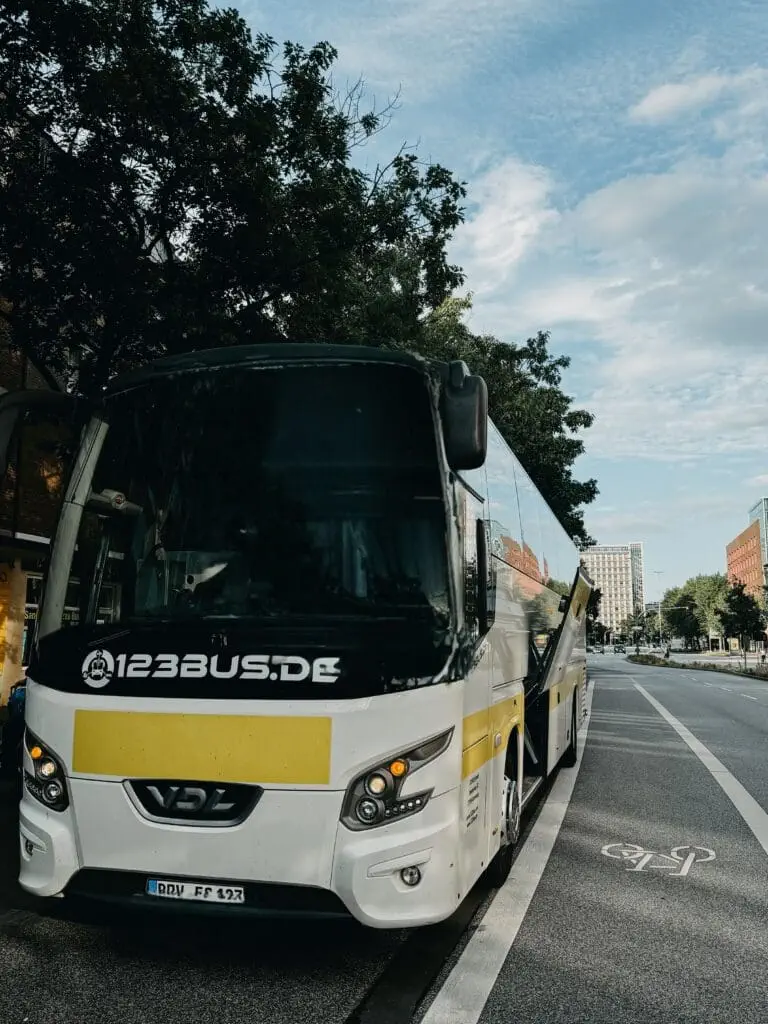 weißer Reisebus mit gelben Streifen und dem Schriftzug 123bus auf der Frontseite am Straßenrand stehend