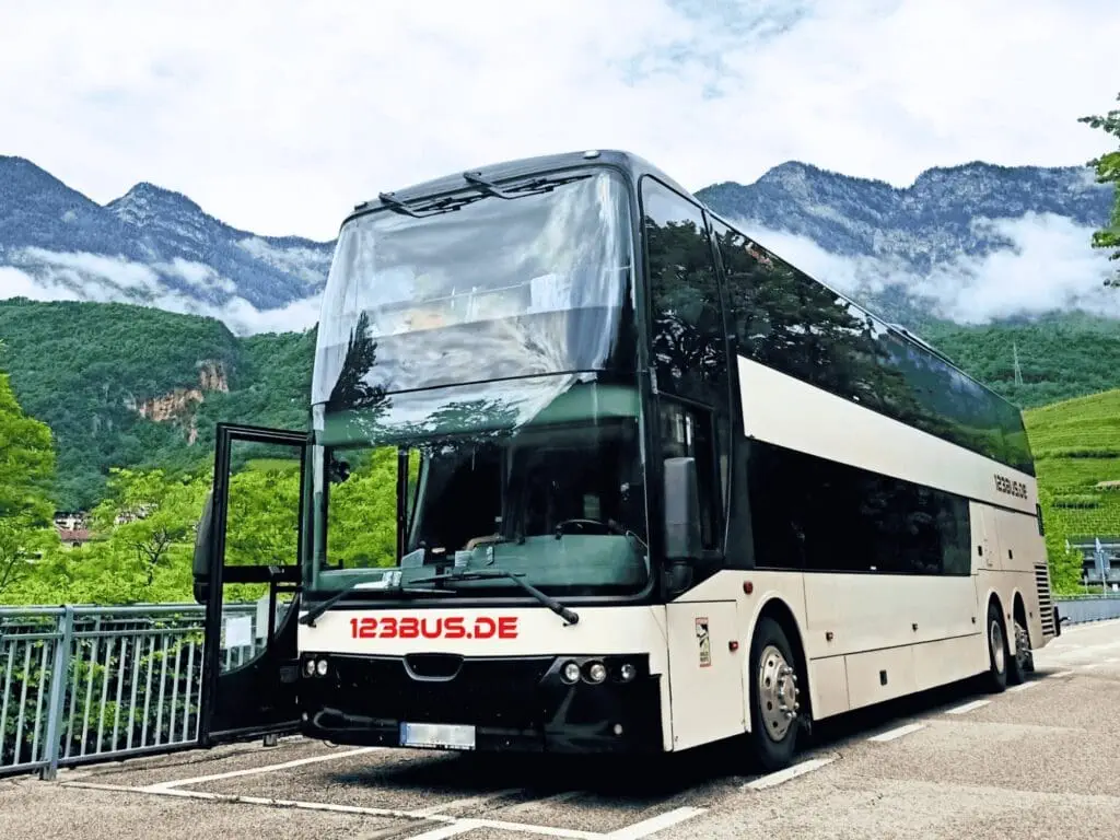 weißer Doppeldeckerreisebus mit rotem Schriftzug 123bus.de in einer italienischen Landschat mit Bergen im Hintergrund